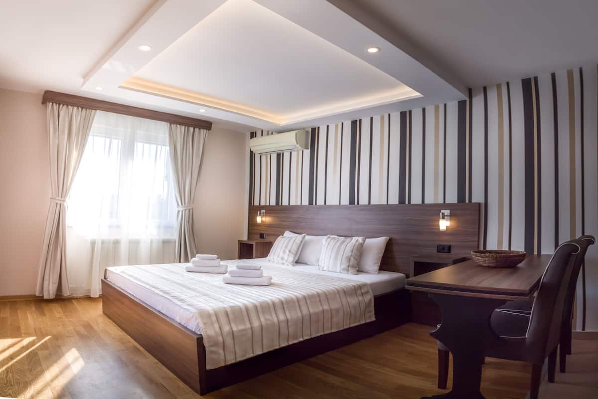 A modern hotel room with a large bed, a wooden desk, and a striped wall.