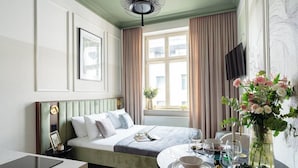 A hotel room with a bed, bedside table, window with curtains, a vase with flowers, and a television on the wall. - Garden Palace - Loftaffair Collection (Kraków)