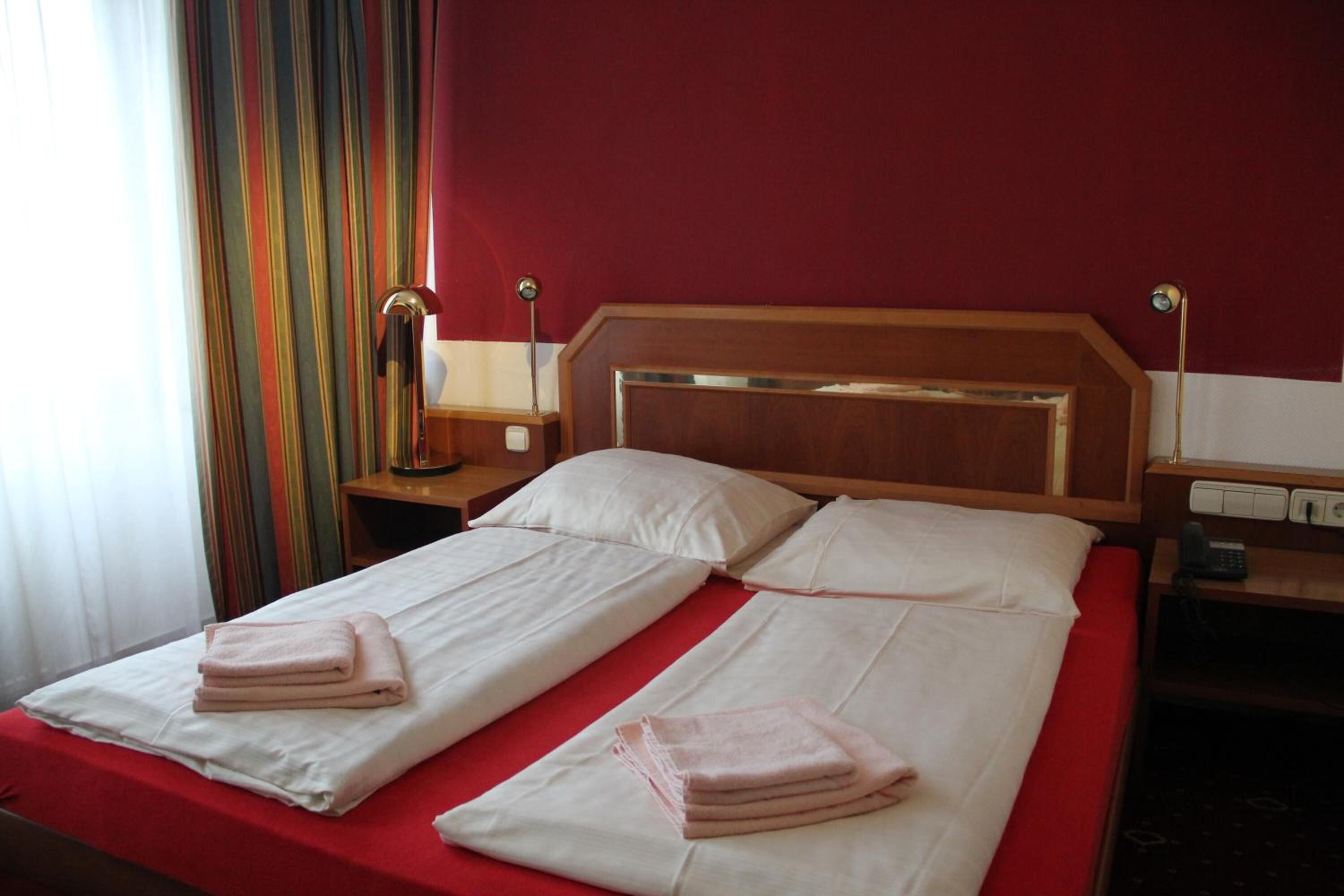 Un lit double avec une literie rouge, deux tables de chevet avec des lampes et un rideau à rayures.