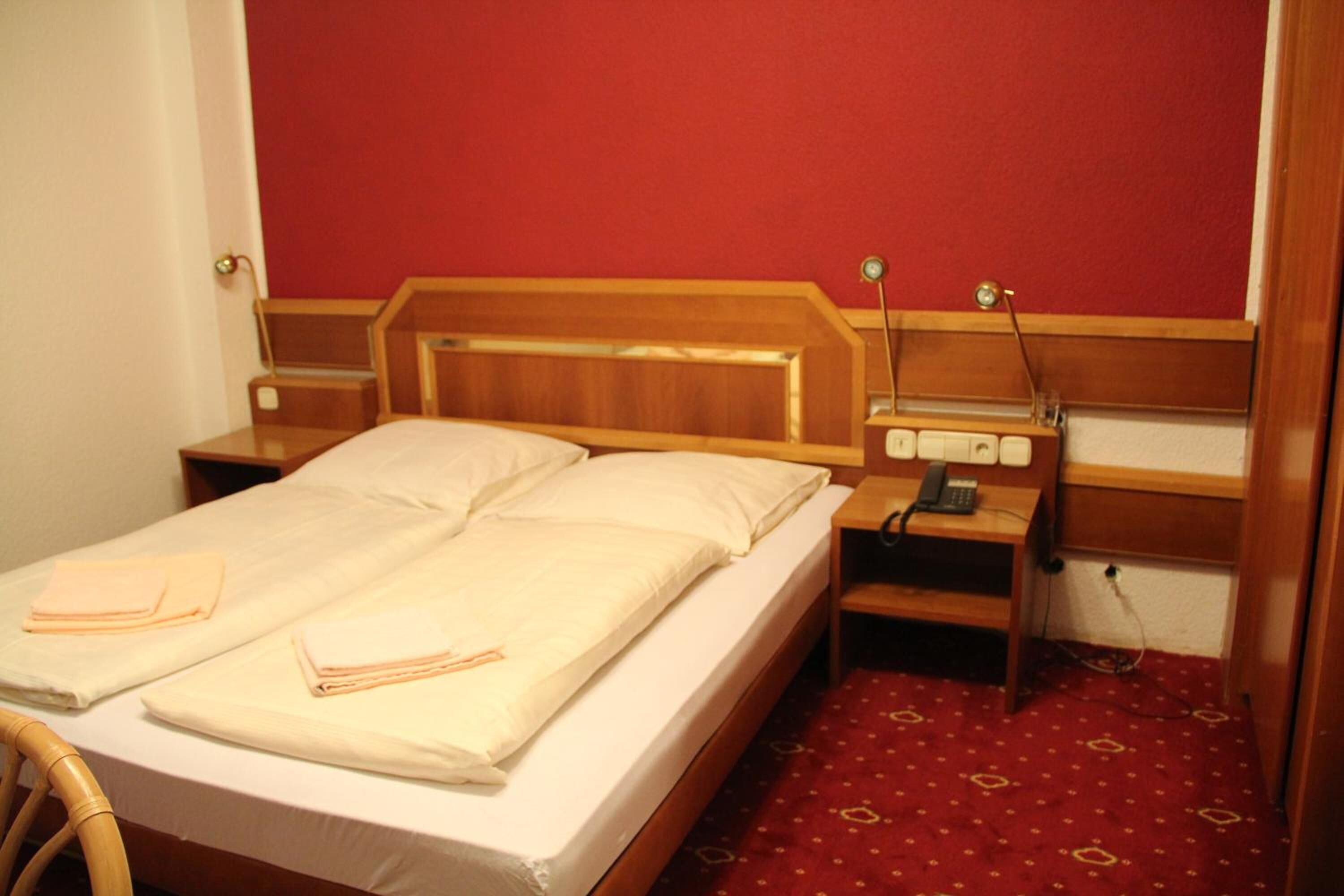 A double bed with a wooden headboard, two bedside tables with lamps, and a red carpeted floor.