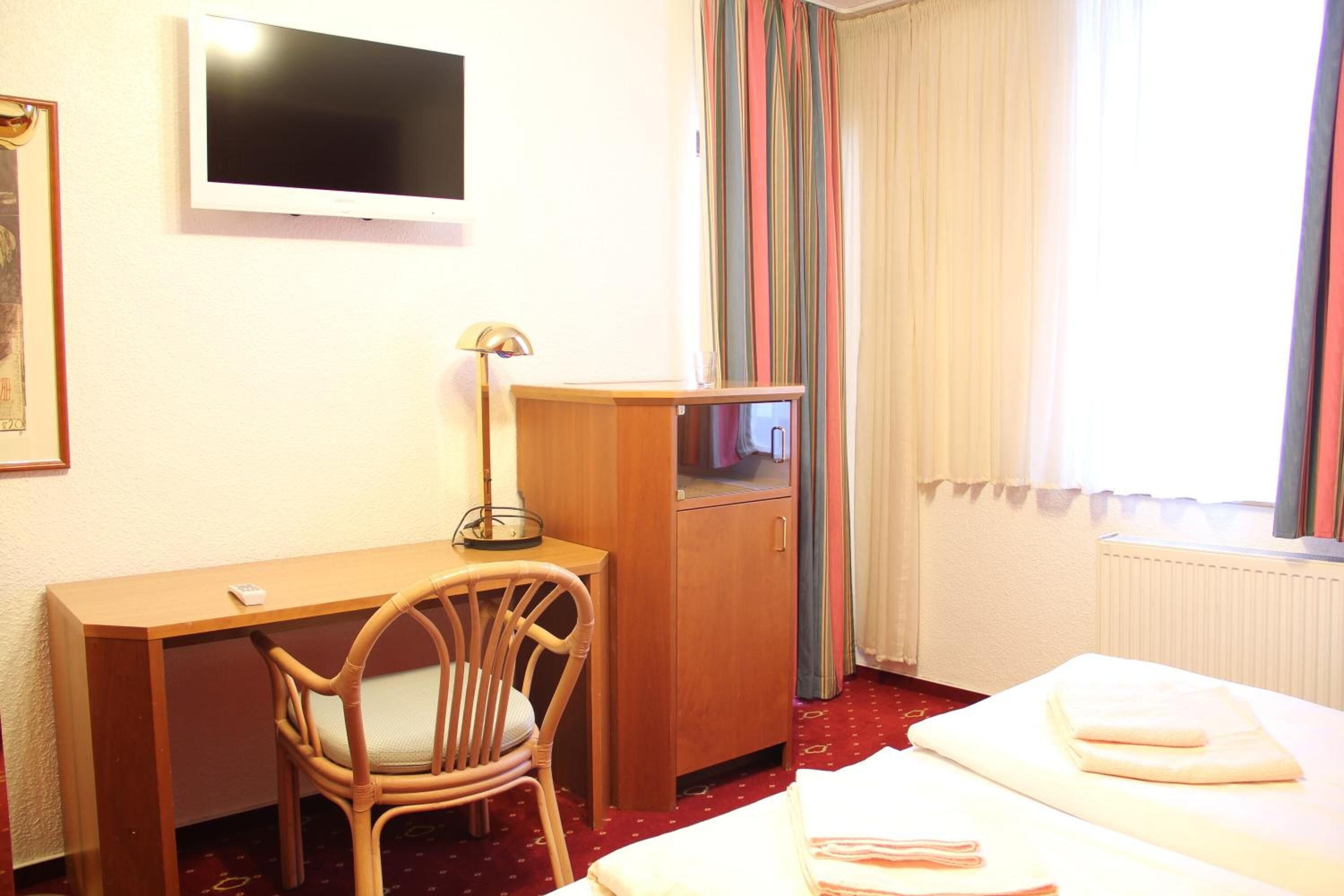 A hotel room with a bed, a desk, a chair, a TV, and a window with curtains.