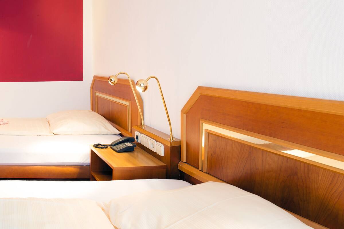 A hotel room with two beds, a wooden headboard, a bedside table with a lamp, and a telephone.