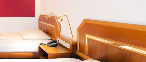 A hotel room with two beds, a wooden headboard, a bedside table with a lamp, and a telephone.