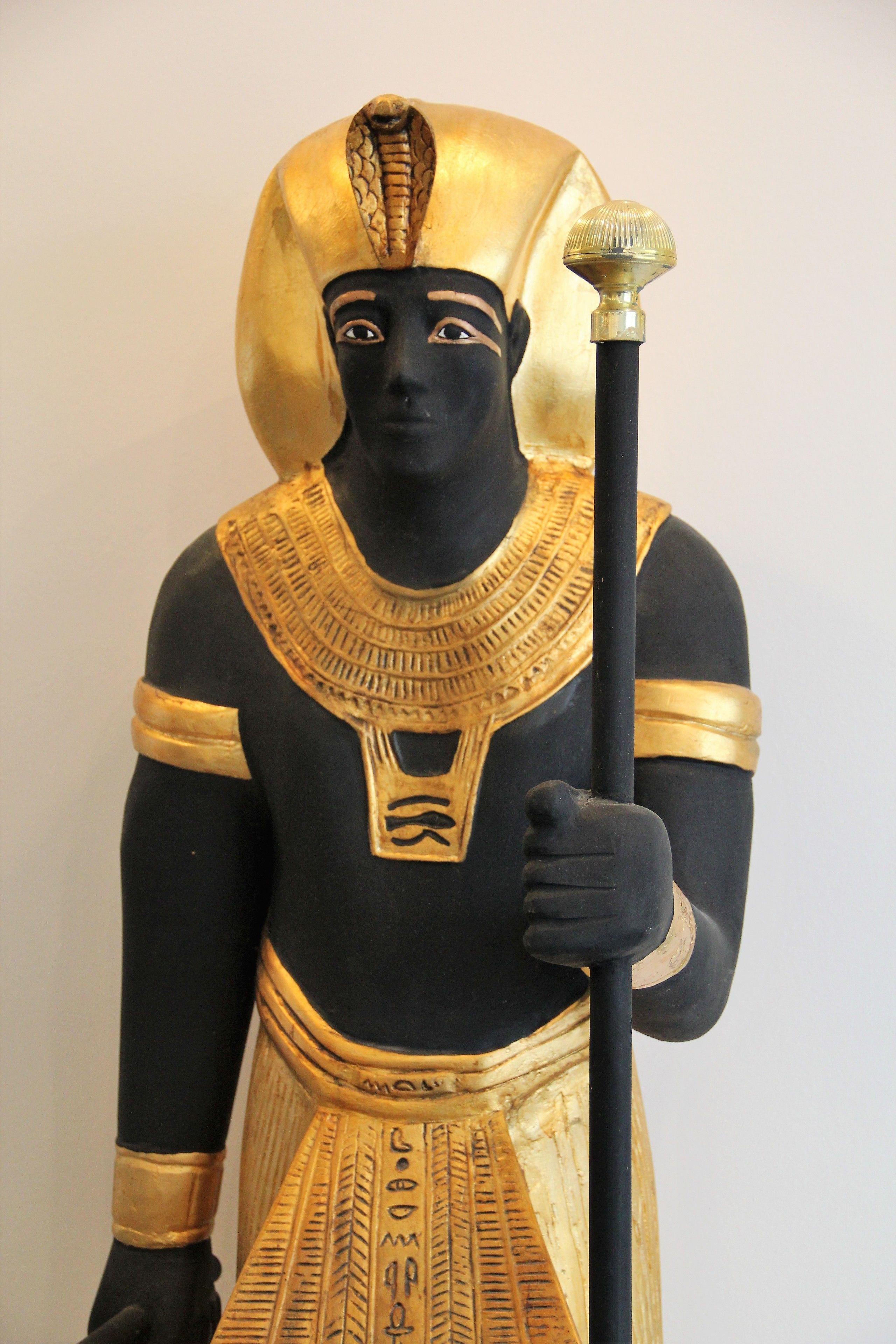 Eine Statue einer Figur in traditioneller altägyptischer Kleidung, darunter eine Kopfbedeckung und ein Stab.