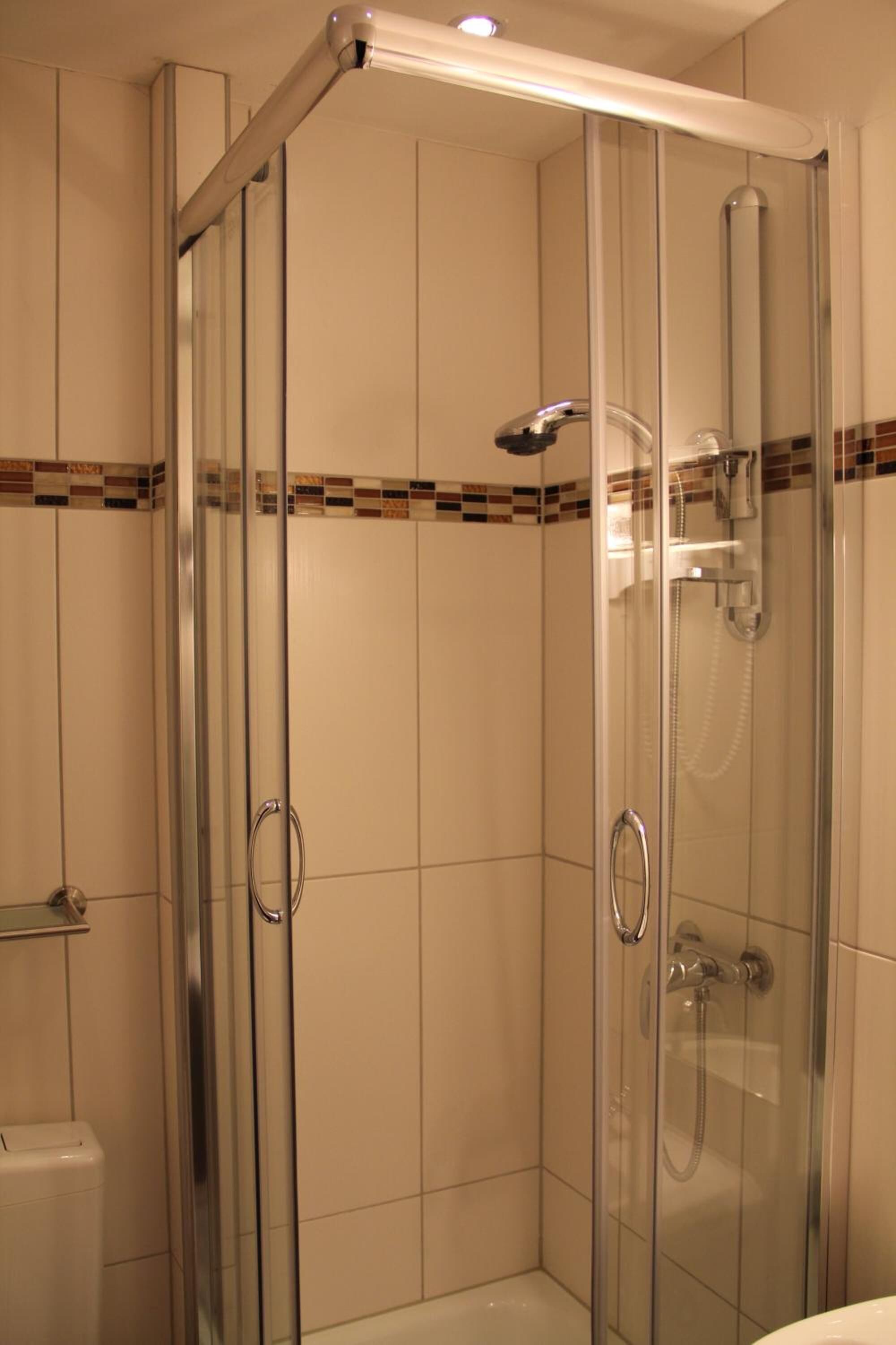 Une cabine de douche fermée par des parois en verre, dotée d’un pommeau de douche à main et d’un robinet fixé au mur.