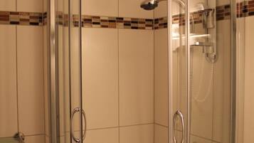 A glass-enclosed shower stall with a handheld showerhead and a wall-mounted faucet.