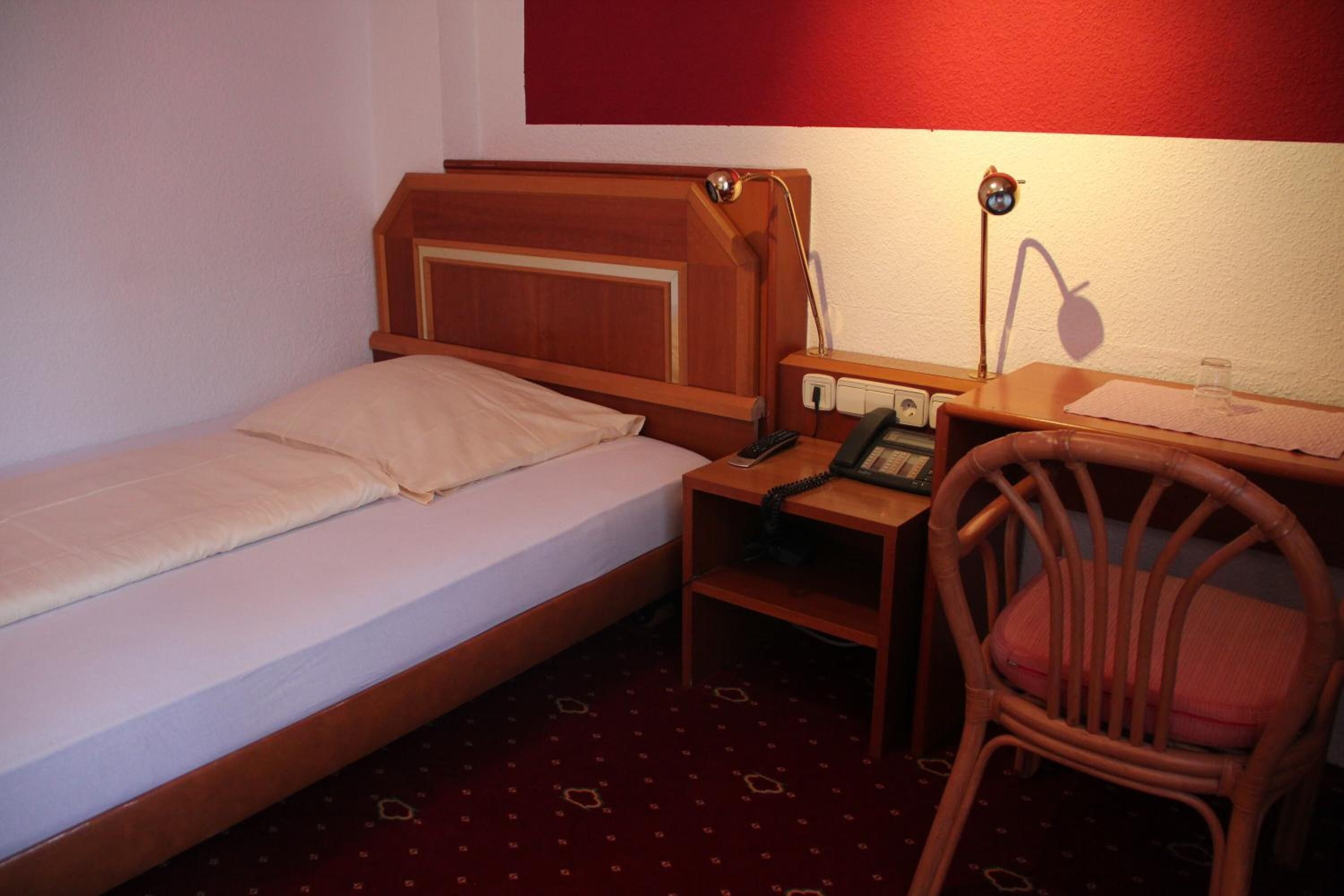 A small, single-bed room with a wooden headboard, a desk with a telephone, and a chair.