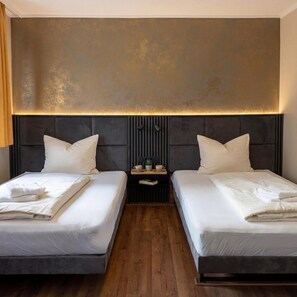 A hotel room with two beds, a wooden floor, a modern headboard, and a nightstand with a lamp and a small table. - Hotel Wali (Bielefeld)