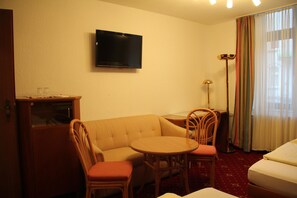A hotel room with a sofa, two chairs, a small table, a TV, a desk, and a bed. - Hotel Wali (Bielefeld)