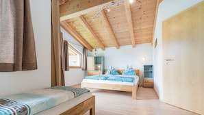 Un dormitorio con techo de madera, una cama con ropa de cama estampada, un banco, un armario y una mesita.
