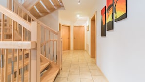 Un pasillo con una escalera de madera, suelo de baldosas y tres cuadros en la pared.