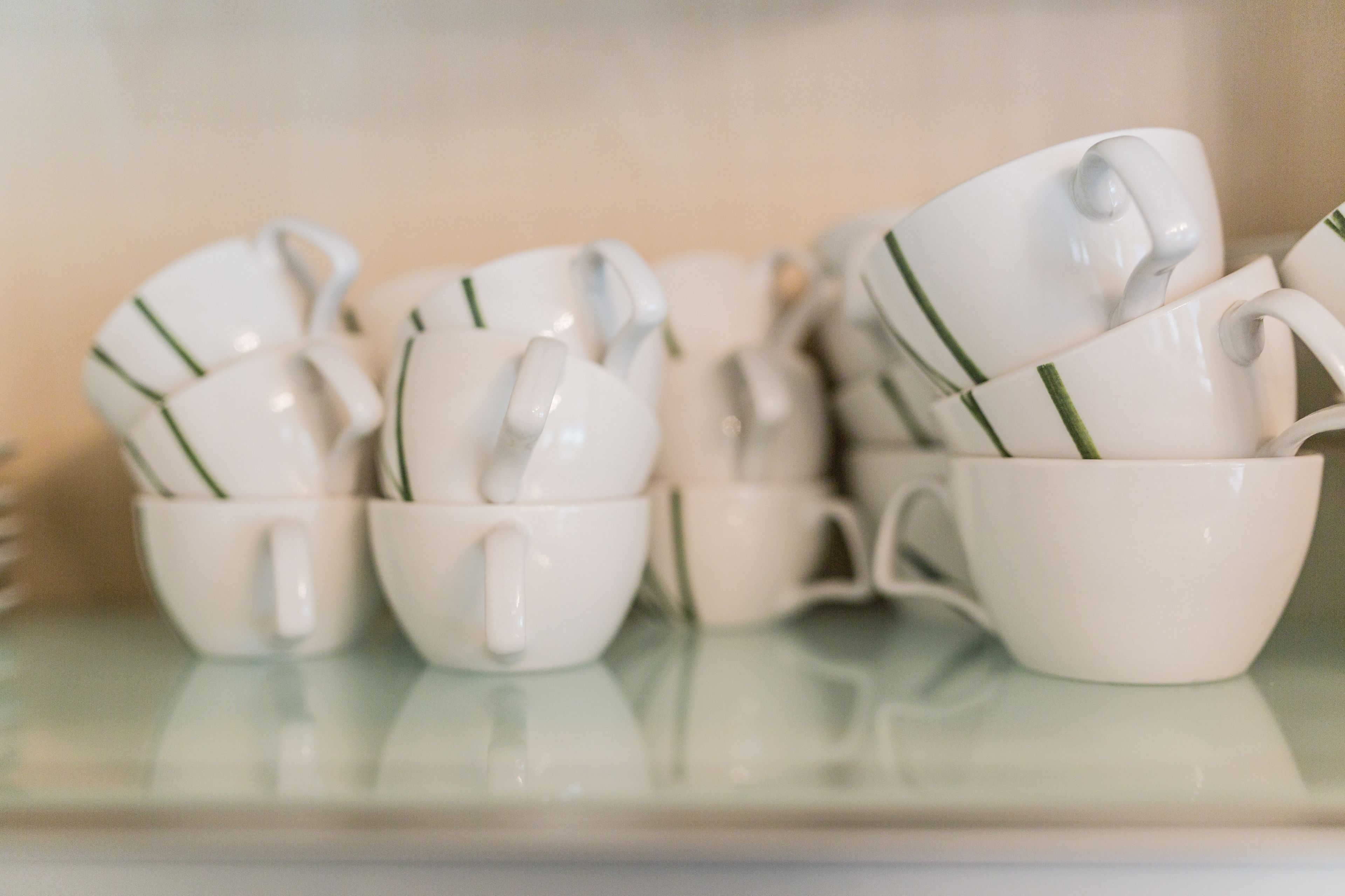 Une collection de tasses en céramique blanche à rayures vertes, posées sur une surface réfléchissante.