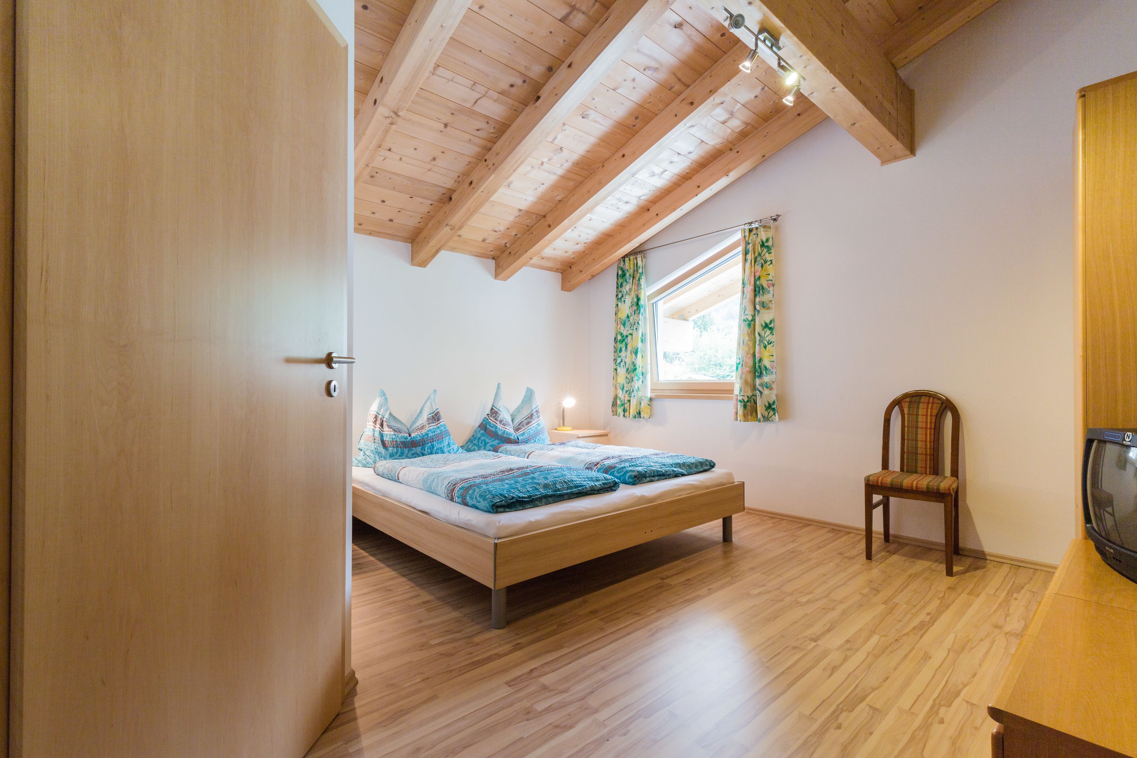 A bedroom with a wooden bed, a chair, and a television.