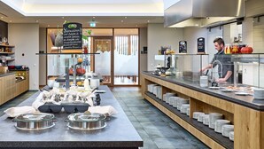 A modern kitchen area with a buffet setup, including a central serving counter with food items and a person preparing food.
