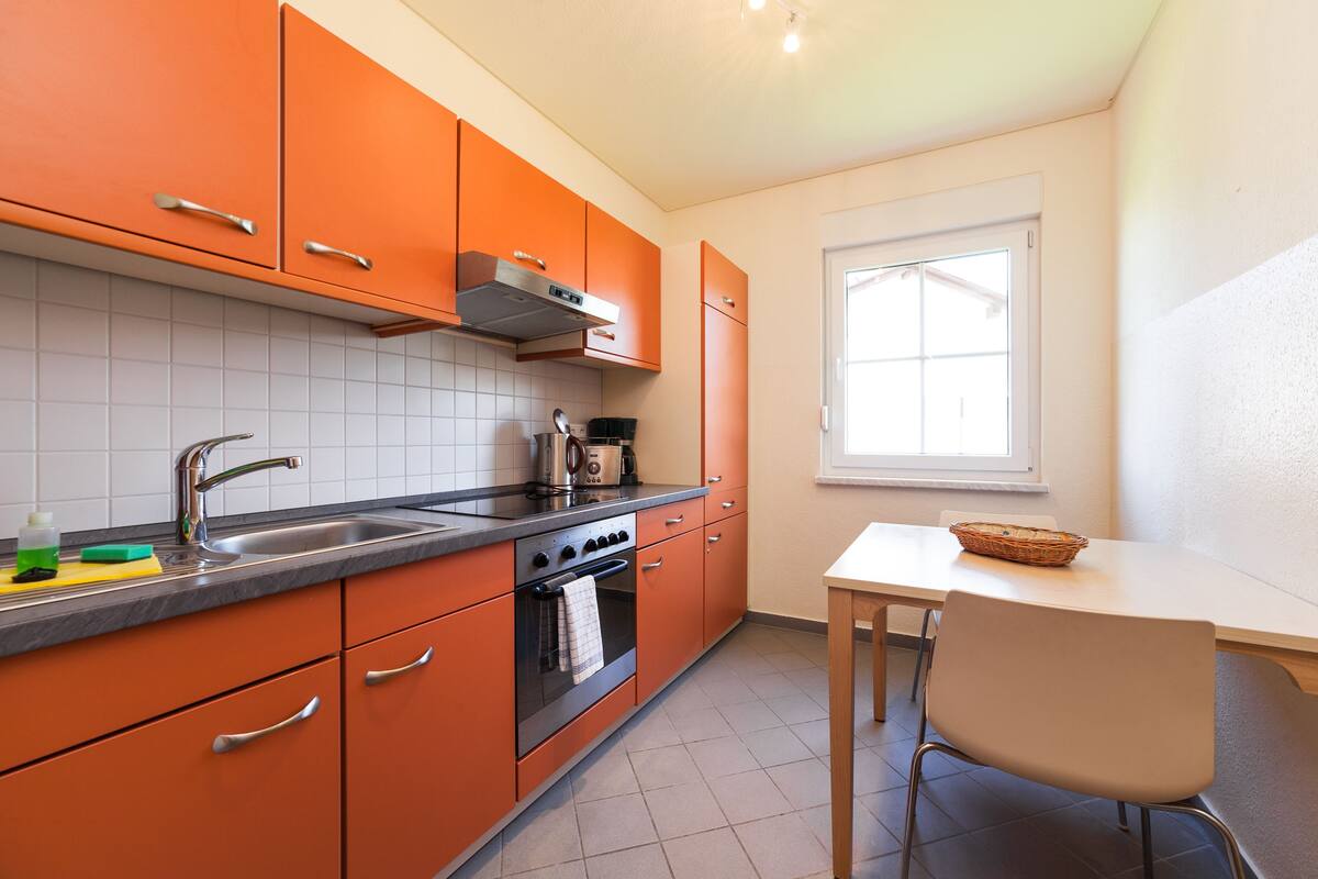 Una cocina con armarios color naranja, un lavamanos de acero inoxidable y un salpicadero blanco con azulejos.