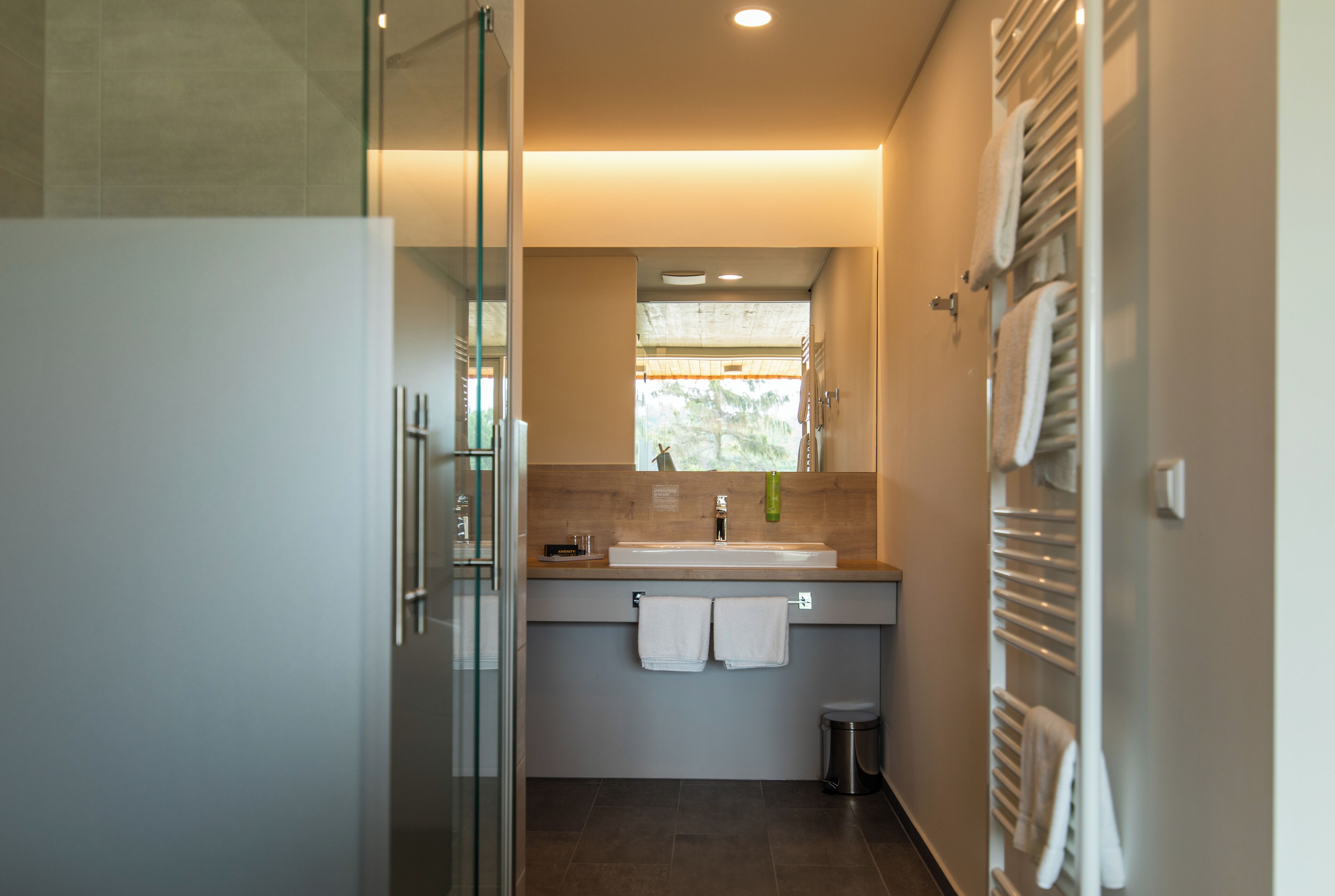 Ein modernes Badezimmer mit Duschkabine aus Glas, Waschbecken mit Spiegel und Handtuchhalter.