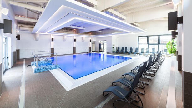 An indoor swimming pool with a modern design, surrounded by lounge chairs and a high ceiling with exposed beams.