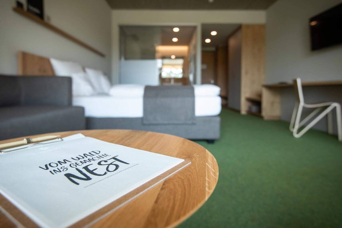 Una habitación de hotel moderna con una mesa de centro de madera, una cama blanca y un sofá gris.