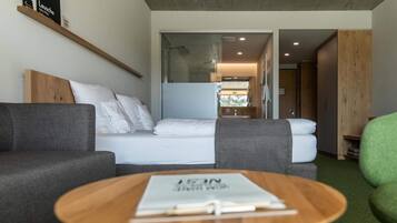 Een moderne hotelkamer met een bed, een grijze bank, een houten bijzettafeltje en uitzicht op de badkamer.
