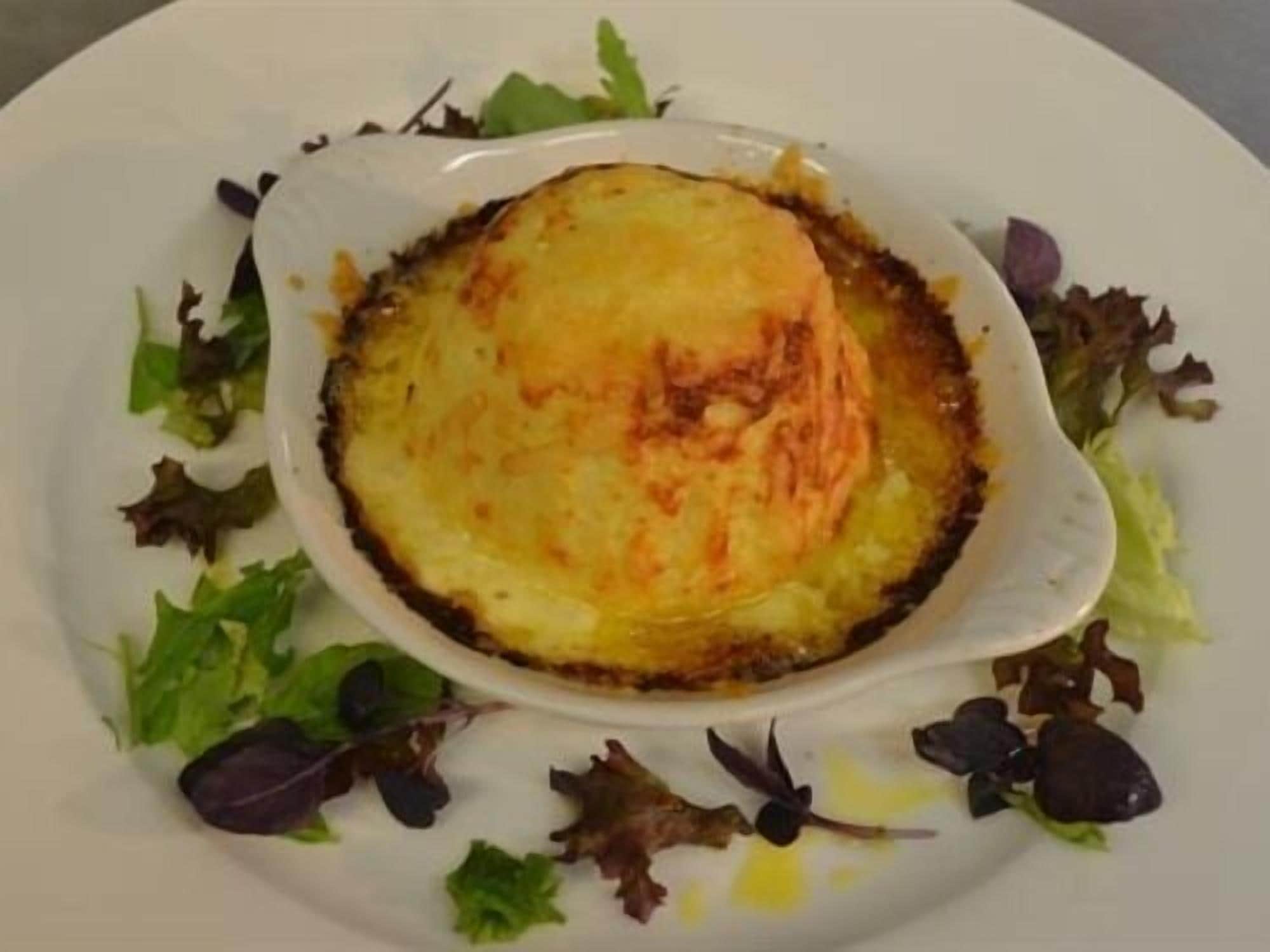 A dish of baked potatoes with a golden-brown crust, surrounded by mixed greens on a white plate.