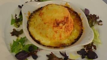 A dish of baked potatoes with a golden-brown crust, surrounded by mixed greens on a white plate.