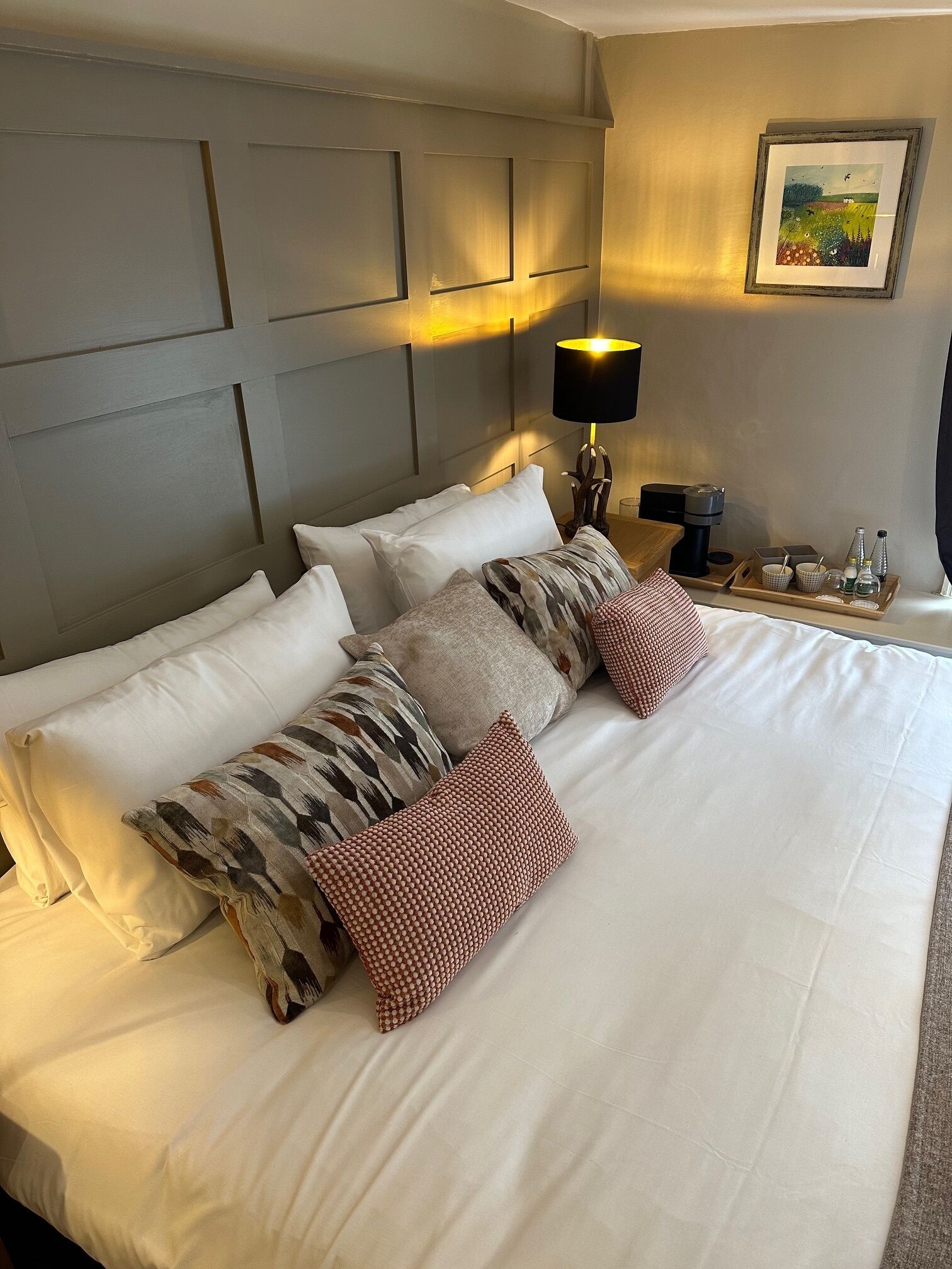 A neatly made bed with white linens and multiple pillows, a bedside table with a lamp, and a framed picture on the wall.