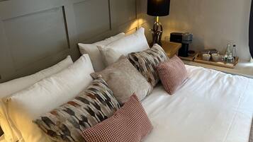 A neatly made bed with white linens and multiple pillows, a bedside table with a lamp, and a framed picture on the wall.