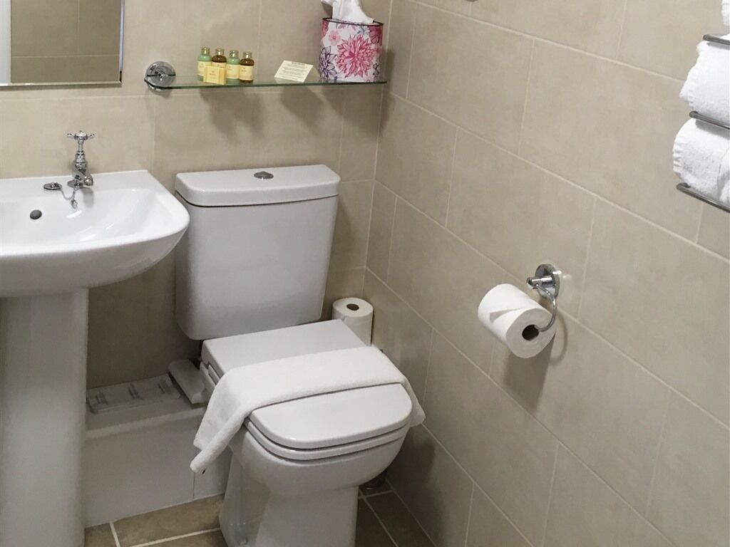 Casa de banho com lavatório branco, sanita e prateleira de vidro com artigos de higiene pessoal.