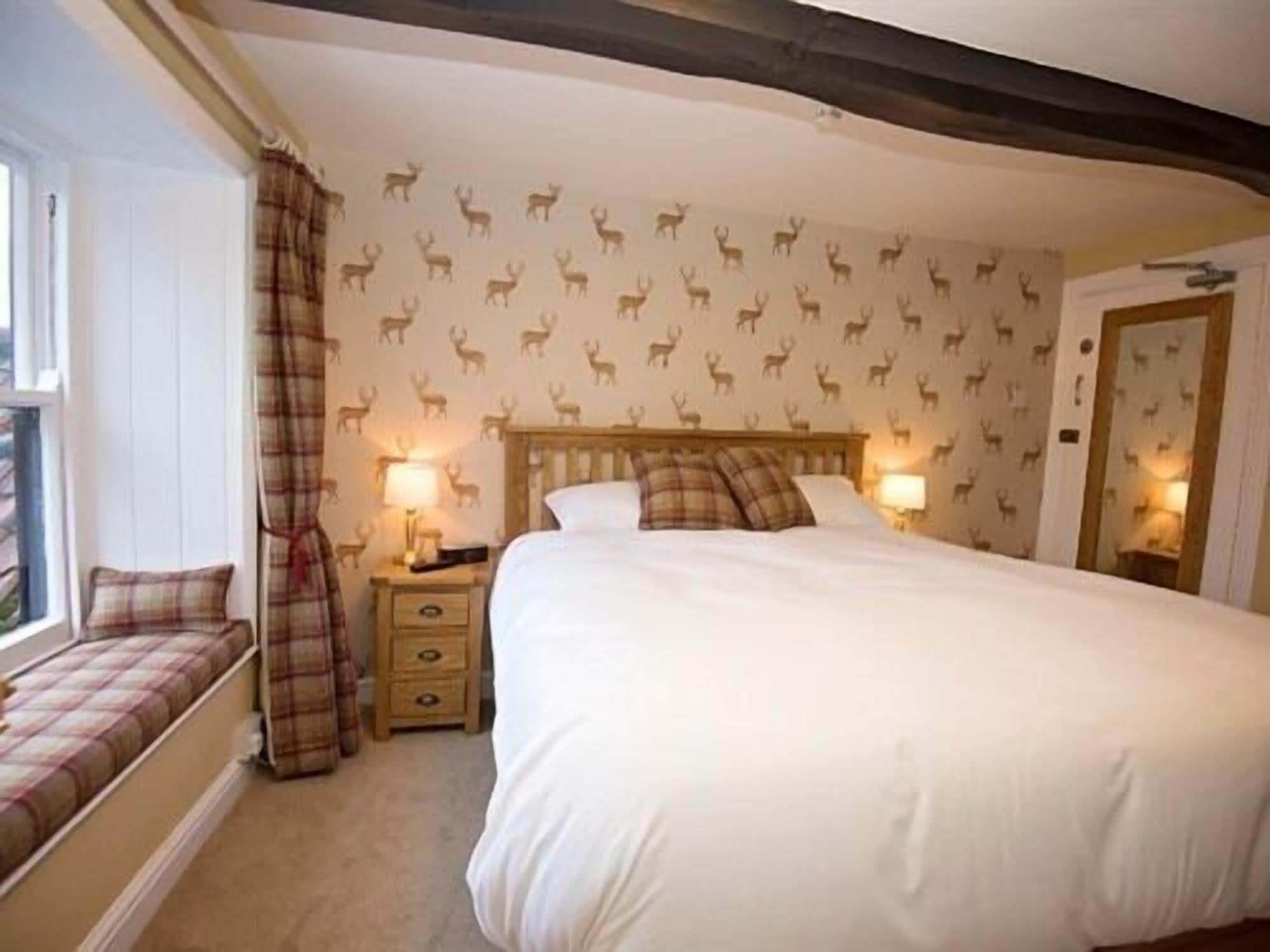 A bedroom with a large bed, two bedside tables, a bench at the window, and a door with a mirror.