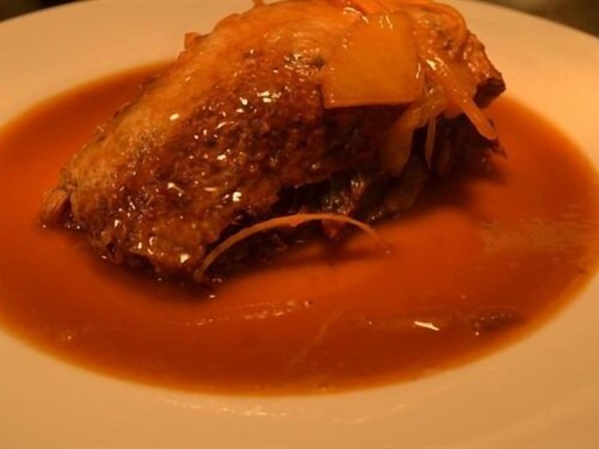 Un plat doté d’une croûte dorée, peut-être un plat rôti ou cuit au four, servi avec une sauce rouge.