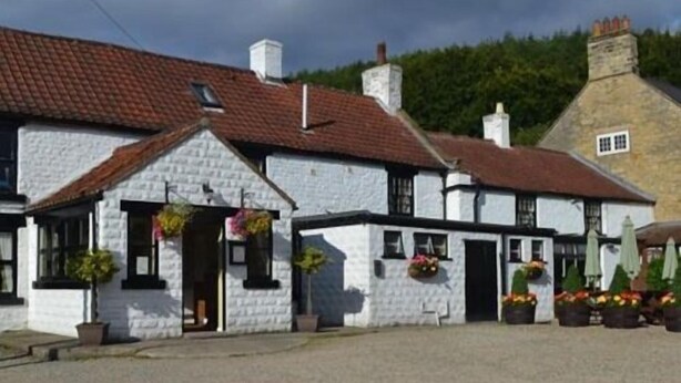 A traditional white building with a red-tiled roof, multiple windows, and hanging flower baskets. - The Stapylton Arms (York)