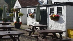 A white building with a tiled roof, outdoor tables, and hanging flower baskets. - The Stapylton Arms (York)