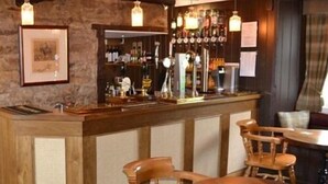 A bar area with wooden furniture, a counter with bottles, and hanging lights. - The Stapylton Arms (York)
