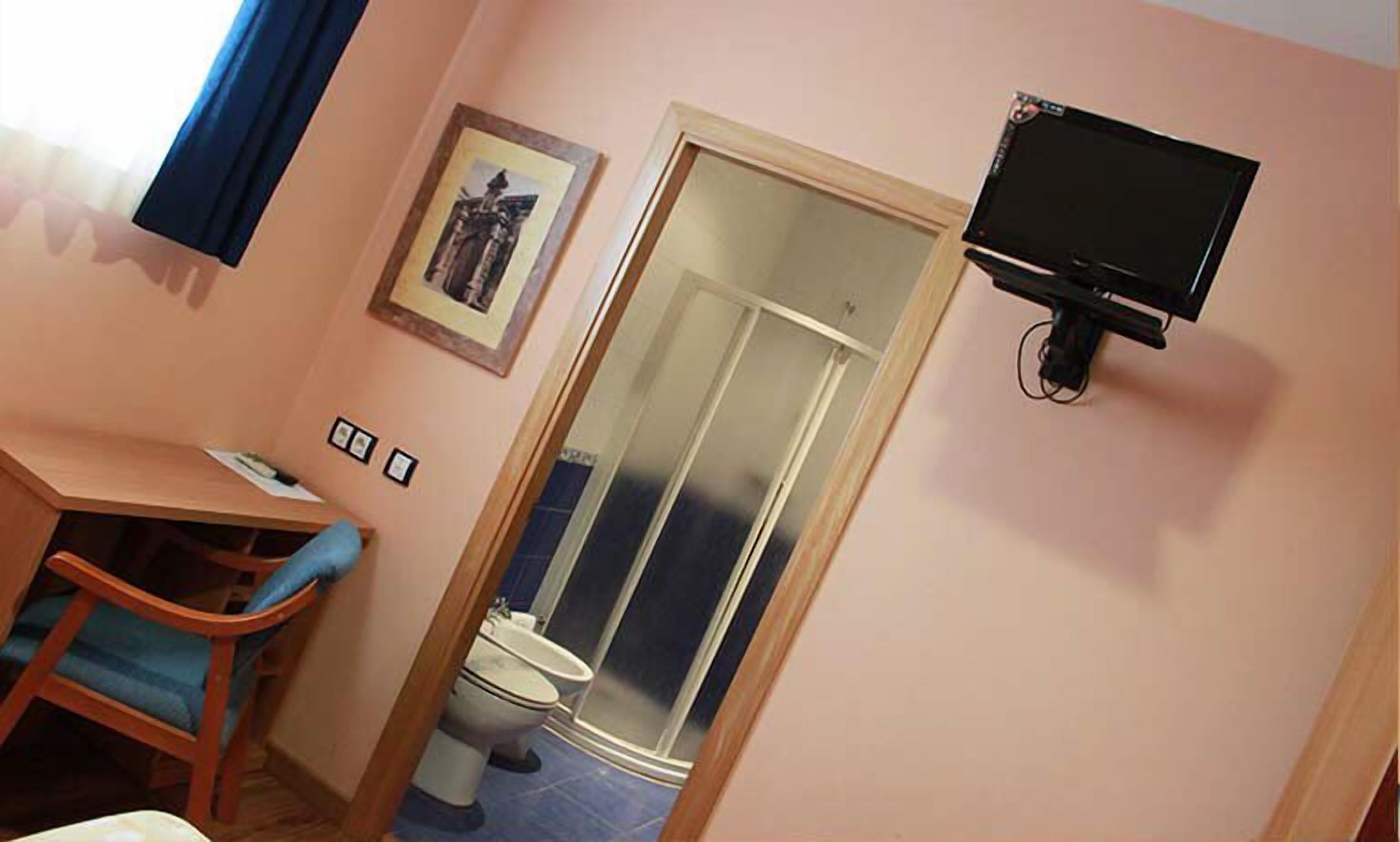 A small room with a desk, chair, toilet, and a television mounted on the wall.