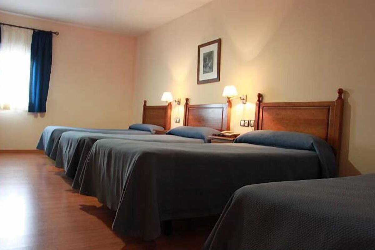 Ein Hotelzimmer mit drei Einzelbetten, Holz-Kopfteilen, Nachttischlampen und einem gerahmten Bild an der Wand.