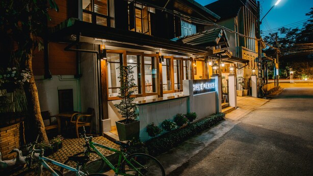 A building with a sign reading "HEUN @ FASHION" at night, featuring a balcony with chairs and a potted plant. - Heun At Fahham (Chiang Mai)