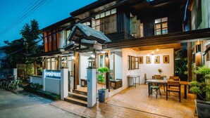 A two-story building with a covered entrance, a patio area with a table and chairs, and a sign that reads "HEIN @ FAHRAM." - Heun At Fahham (Chiang Mai)