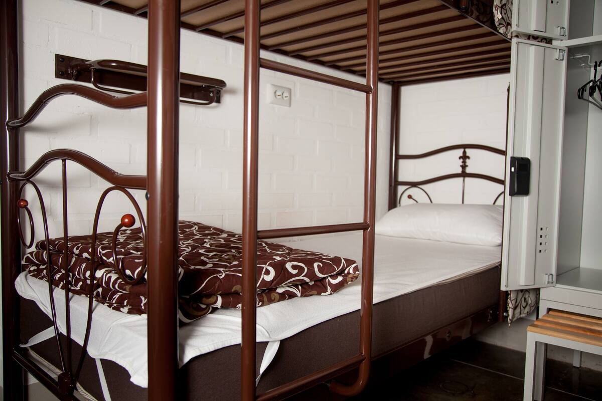 Una cama individual con ropa de cama estampada, cabecera de madera y pared blanca con toma de corriente.