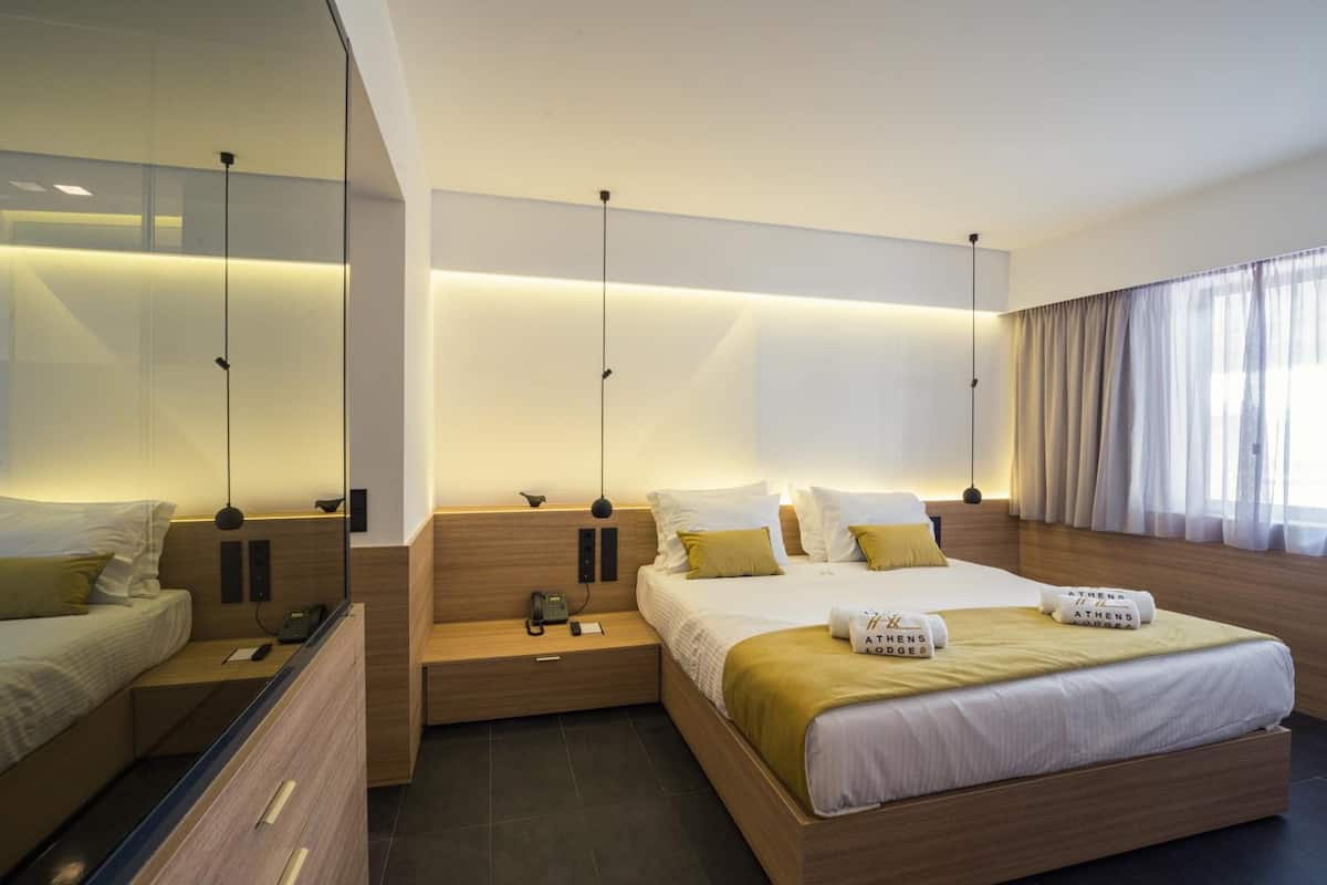 A modern hotel room with a large bed, bedside tables, a mirror, and a large window with curtains.