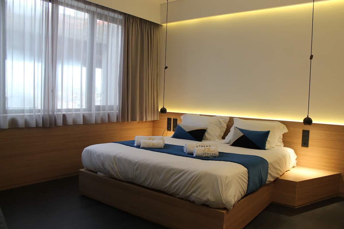 A modern hotel room with a large bed, bedside tables, and a window with curtains.