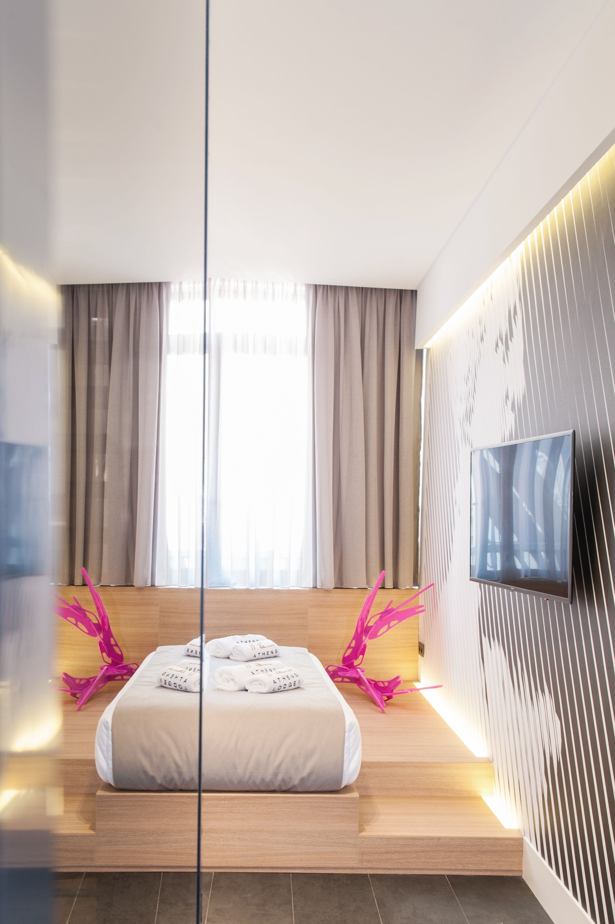 Ein modernes Hotelzimmer mit einem großen Bett, einem flachbildfernseher an der Wand und einem großen Fenster mit Vorhängen.