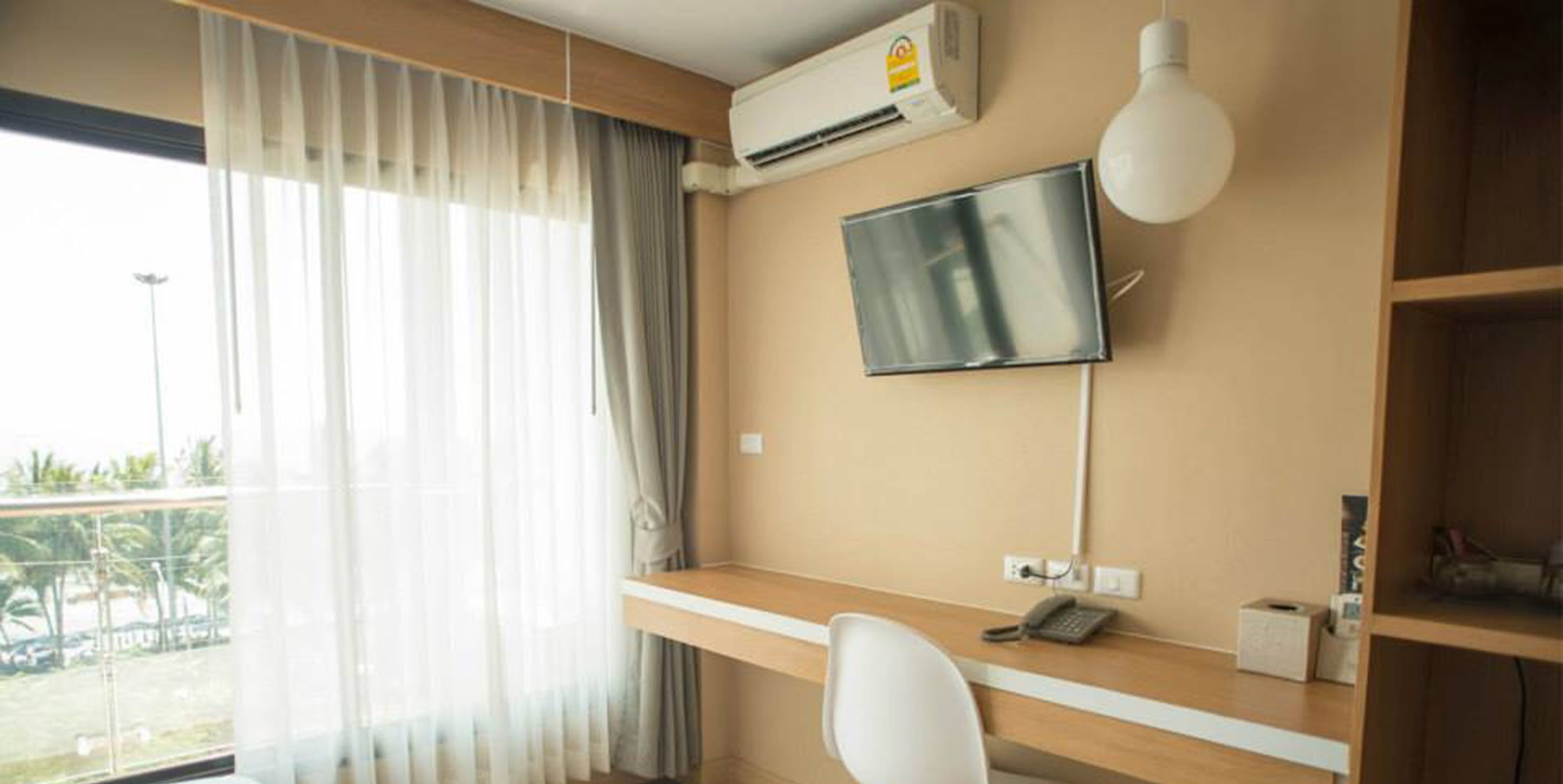 A hotel room with a desk, a television, an air conditioning unit, and a view of the outdoors.