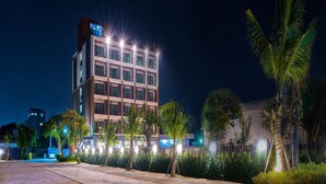 Un hotel moderno con una estructura de varios pisos, ventanas iluminadas y un área exterior bien iluminada con palmeras.