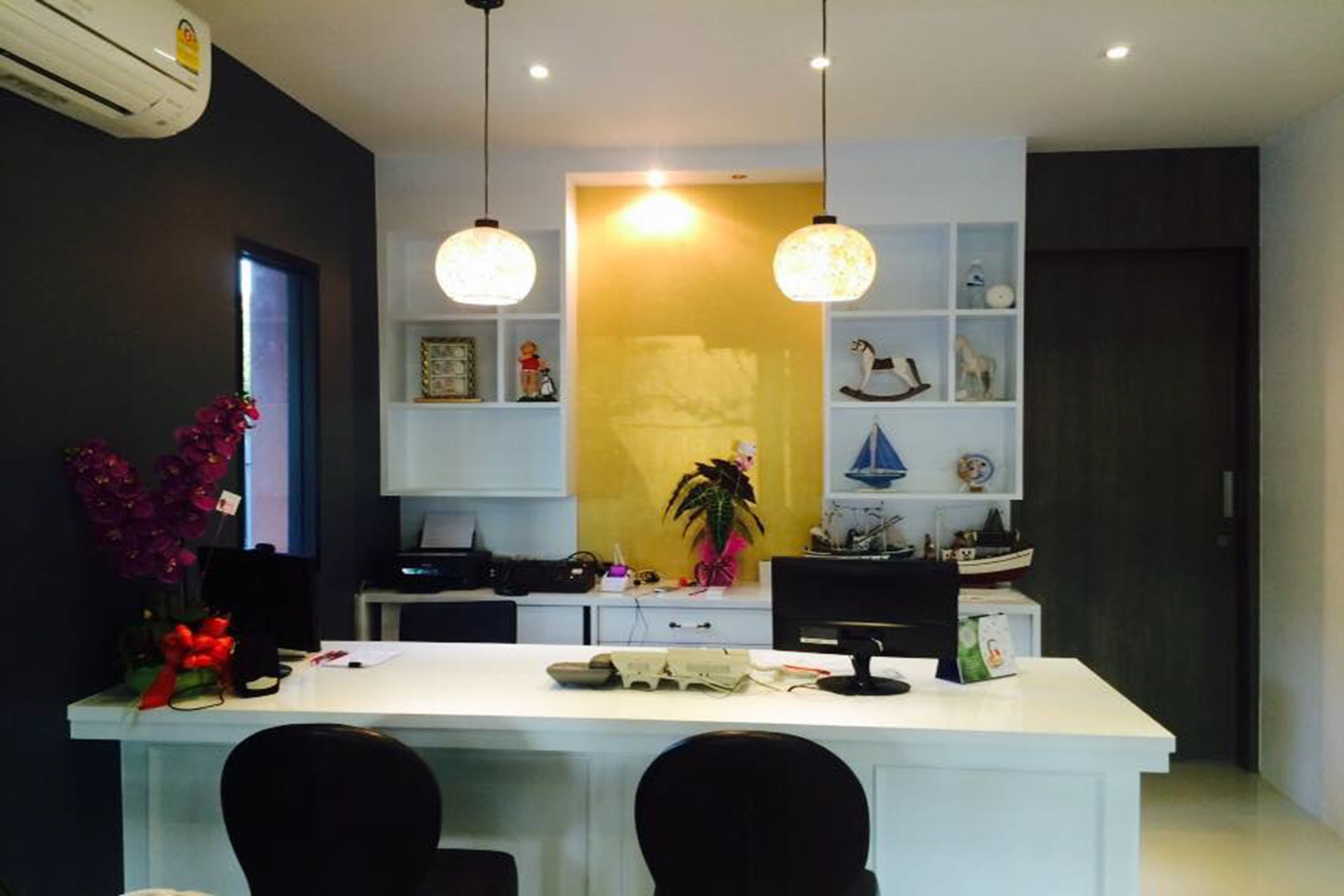 A modern kitchen with a white countertop, black chairs, pendant lights, and decorative items on shelves.