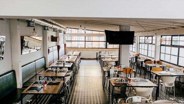 Restaurante com um balcão comprido, cabines e mesas. Há grandes janelas e uma televisão de tela plana na parede.