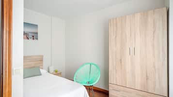 Un dormitorio con una cama, un armario de madera, una silla verde y un cuadro en la pared.