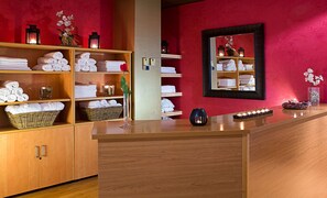 A hotel reception area with wooden cabinets, shelves with folded towels, a vase with flowers, and a mirror on the wall. - Apartamentos Alday (Camargo)