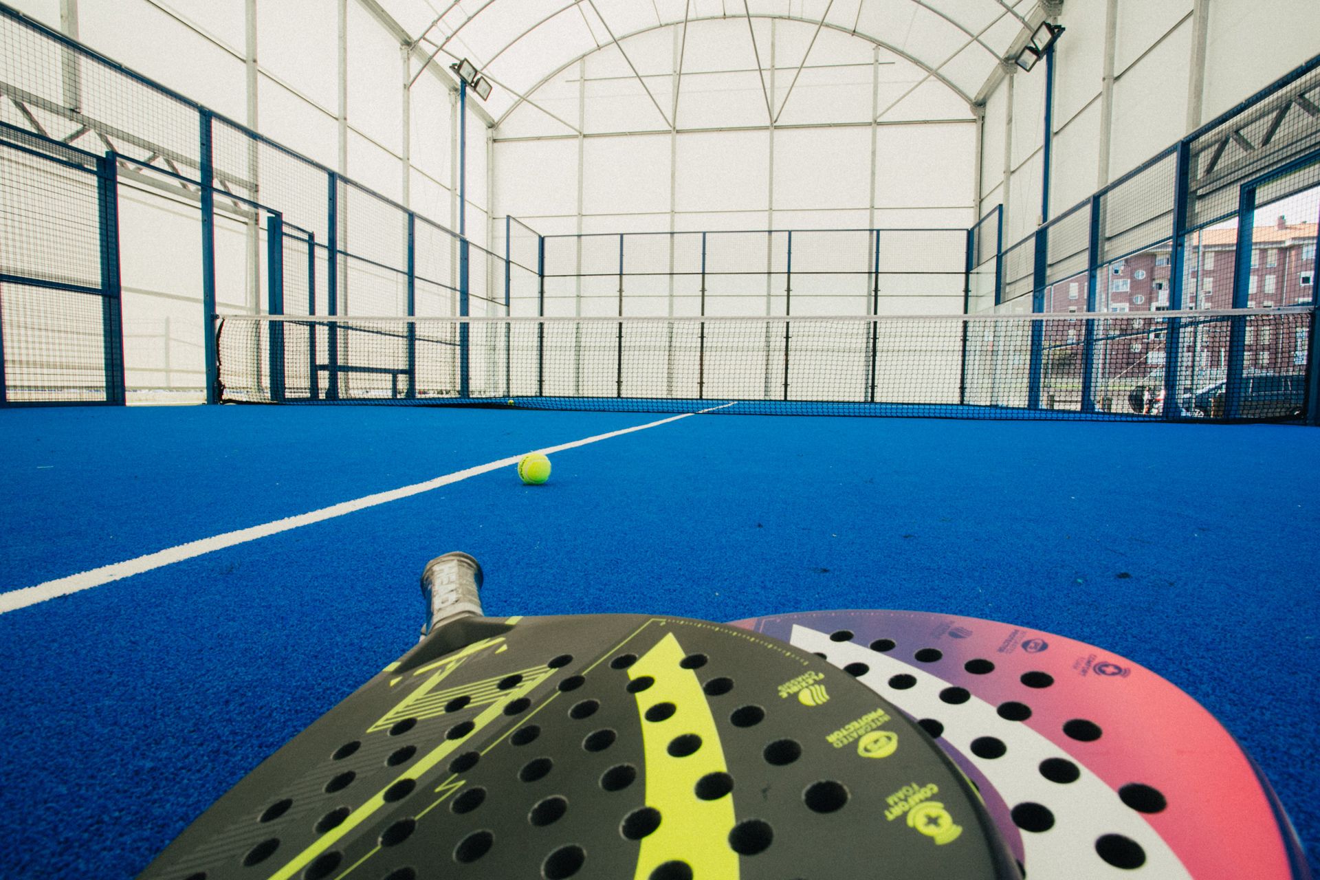 Una palestra coperta con campo da tennis, pavimento blu e linee di delimitazione bianche.