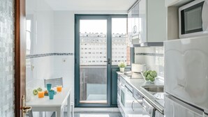 Cozinha compacta com área de refeições, geladeira e vista da cidade através de uma porta de vidro.