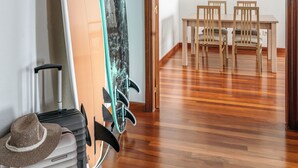 Quarto com dois pranchas de surf encostadas na parede, uma mesa de jantar com cadeiras e chão de madeira.